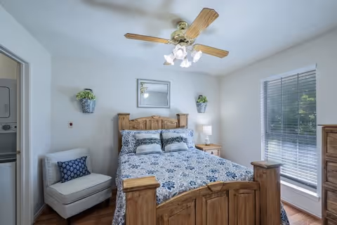 Cozy bedroom with a wooden bed, nightstands, ceiling fan, and large window blinds.