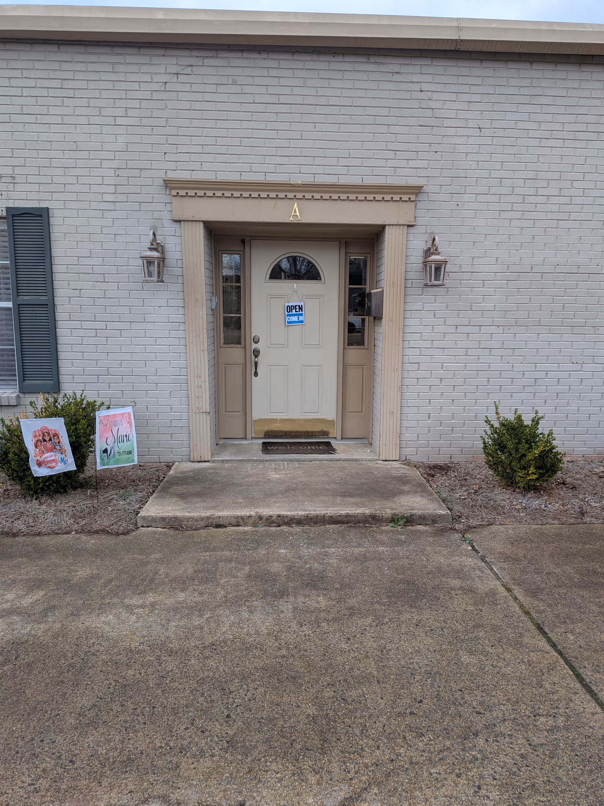 Gray brick building entrance with beige door, lanterns, A above, and open sign.