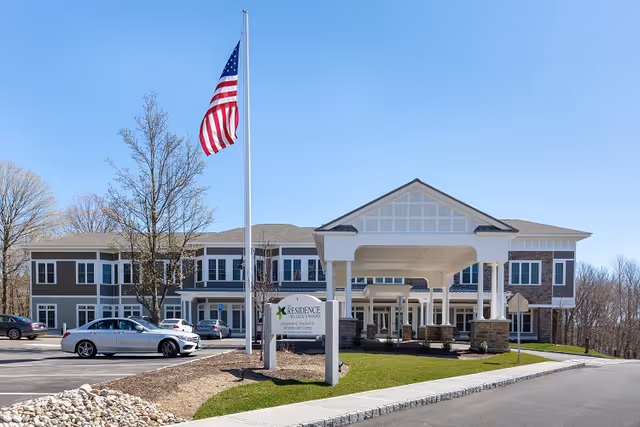 Exterior view of The Residence at Selleck's Woods with porte-cochere entrance and flag.