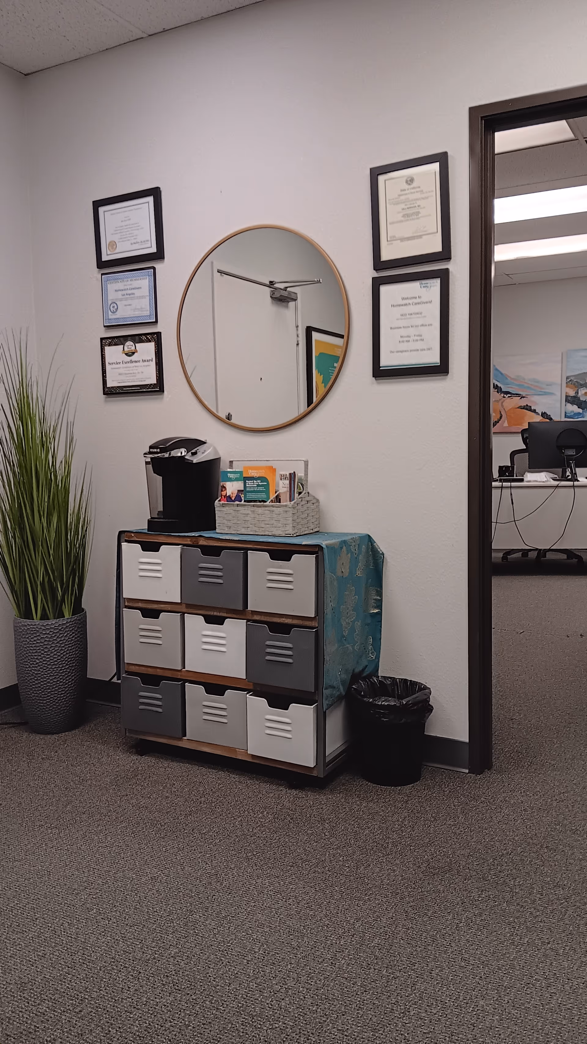Interior hallway with a cabinet, round mirror, framed certificates, and doorway to an office.