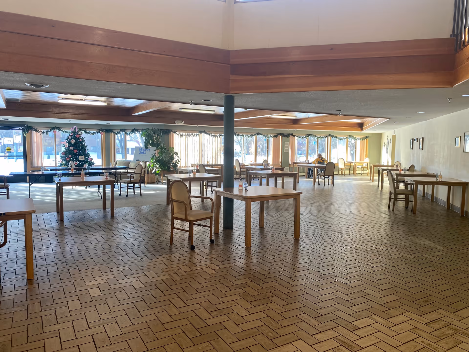 A spacious senior living dining hall with scattered tables, chairs, and holiday decorations.