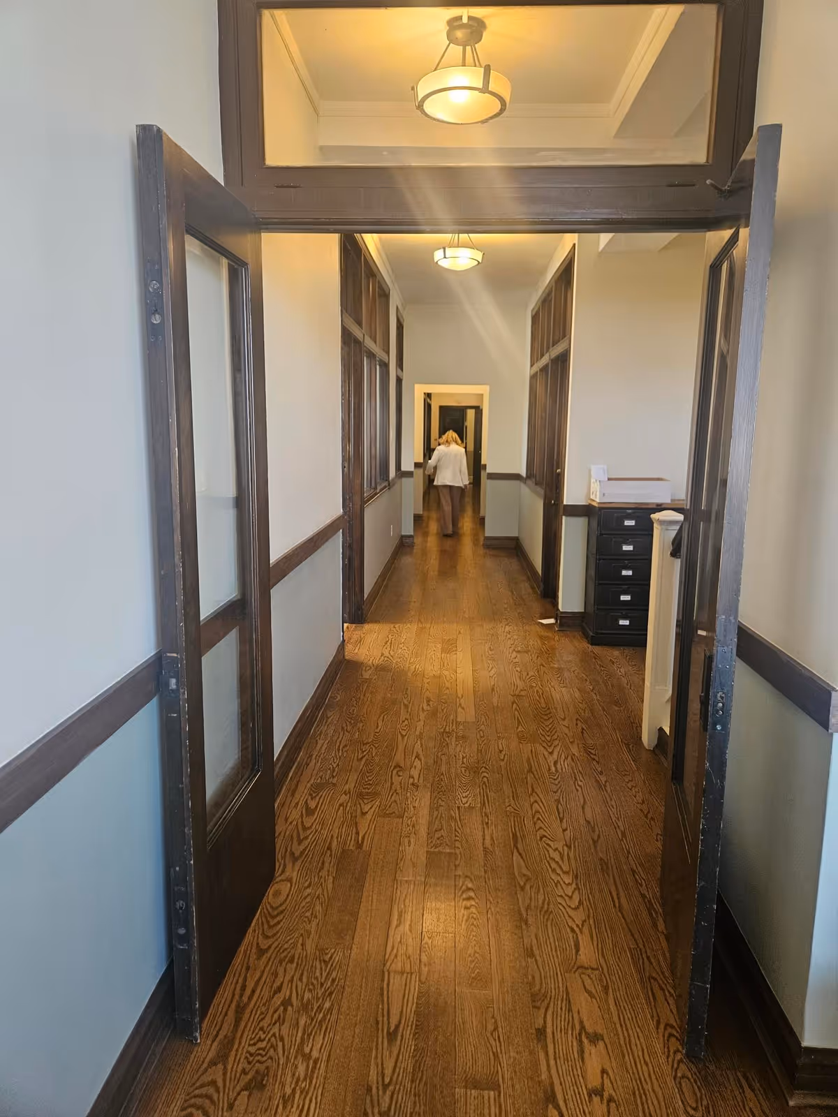 Long wooden hallway in a senior living facility with glass doors and ceiling lights.
