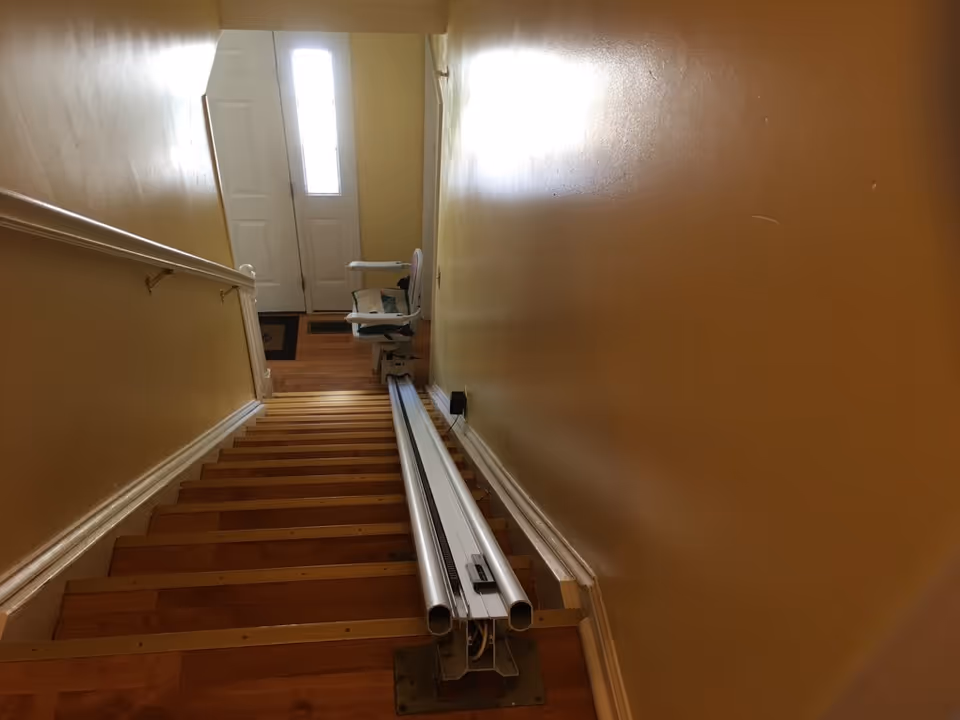 Inside a yellow-walled stairway, a chair lift and railing run along the steps toward a door.