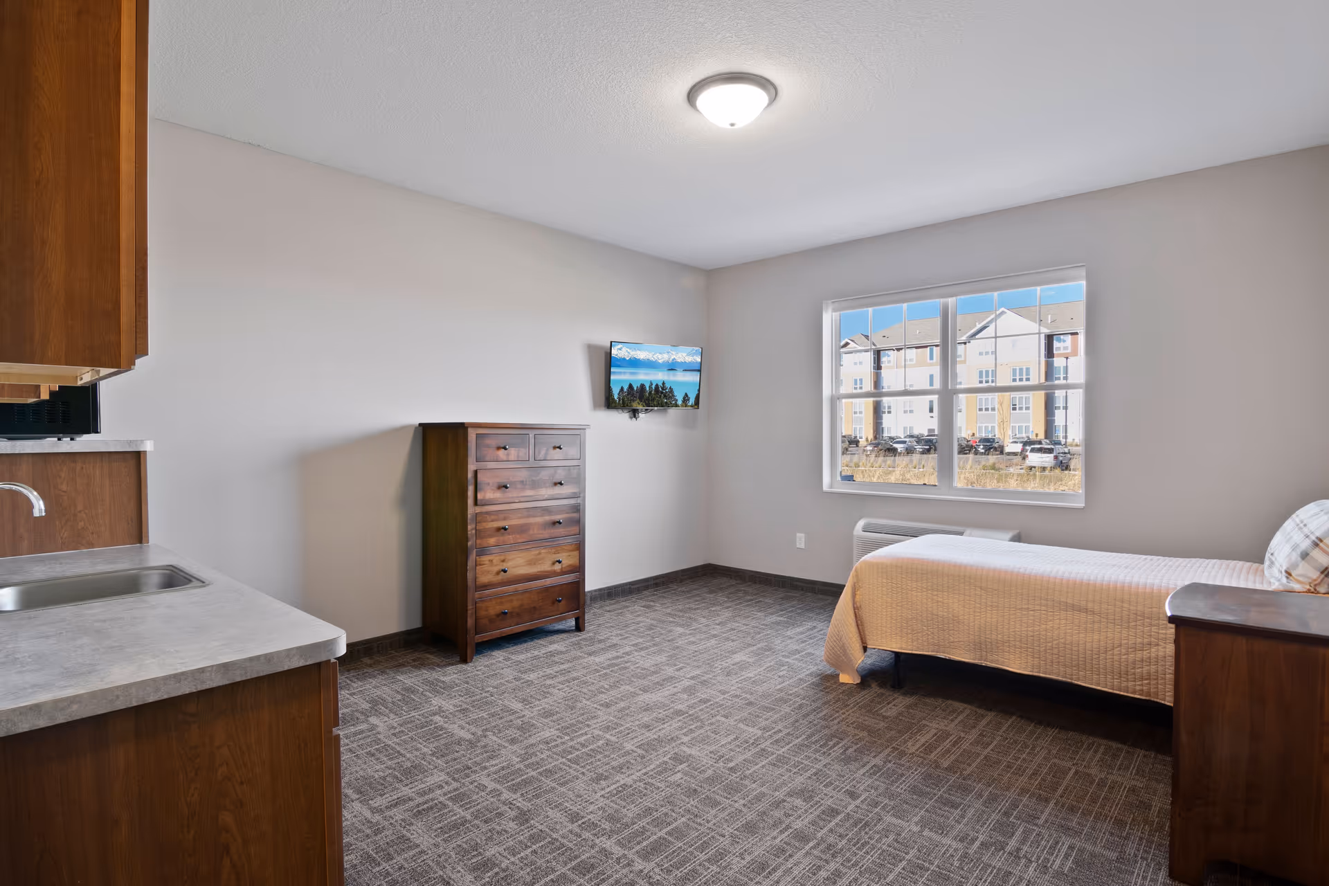 Bedroom suite with bed, dresser, and kitchenette in a neutral-toned, well-lit space.