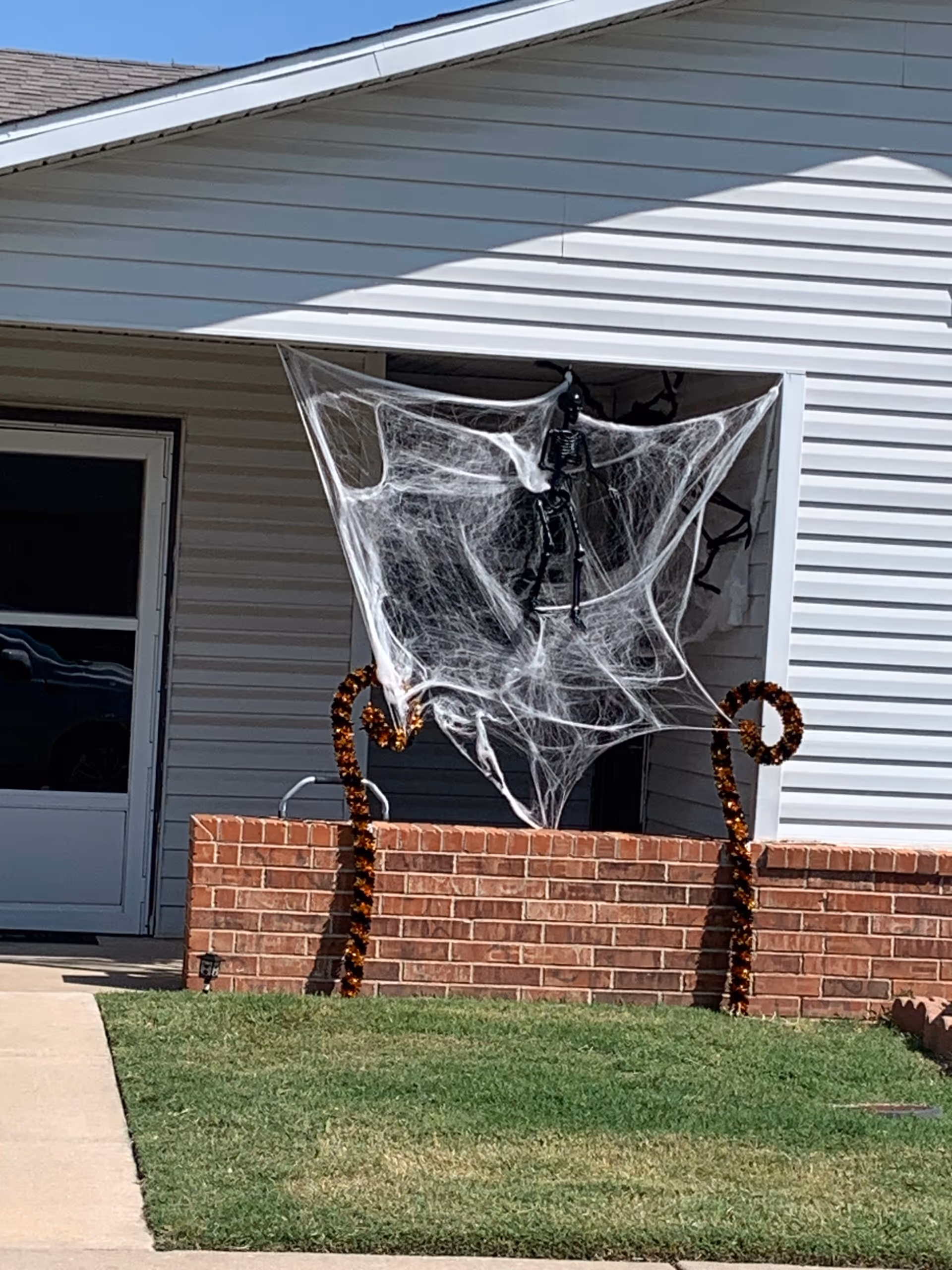 Front exterior of a building with Halloween cobwebs and a hanging spider prop.