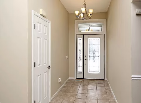 Interior hallway with tiled floor, beige walls, white doors, and a decorative glass front door.