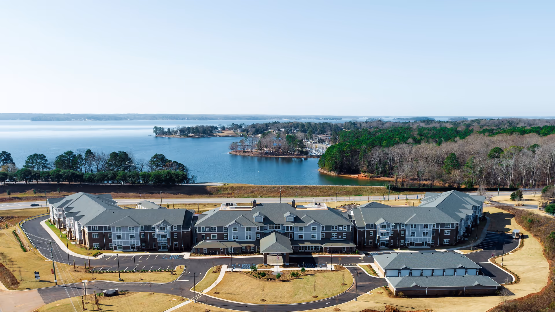Aerial view of a lakeside senior living campus with grey-roofed buildings.