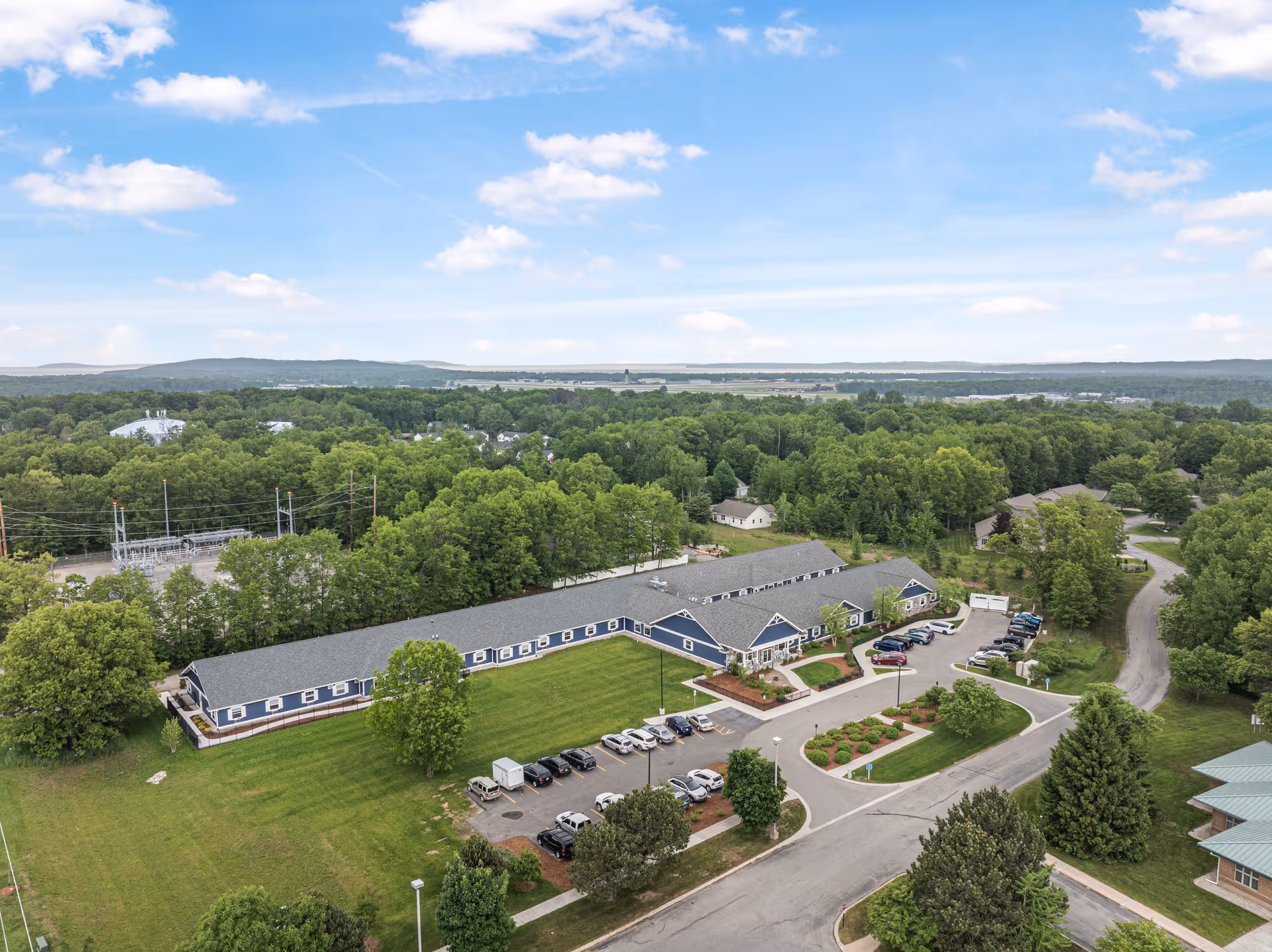 Aerial view of the French Manor Terra building with parking lot, landscaped entrance and surrounding trees and lawns.