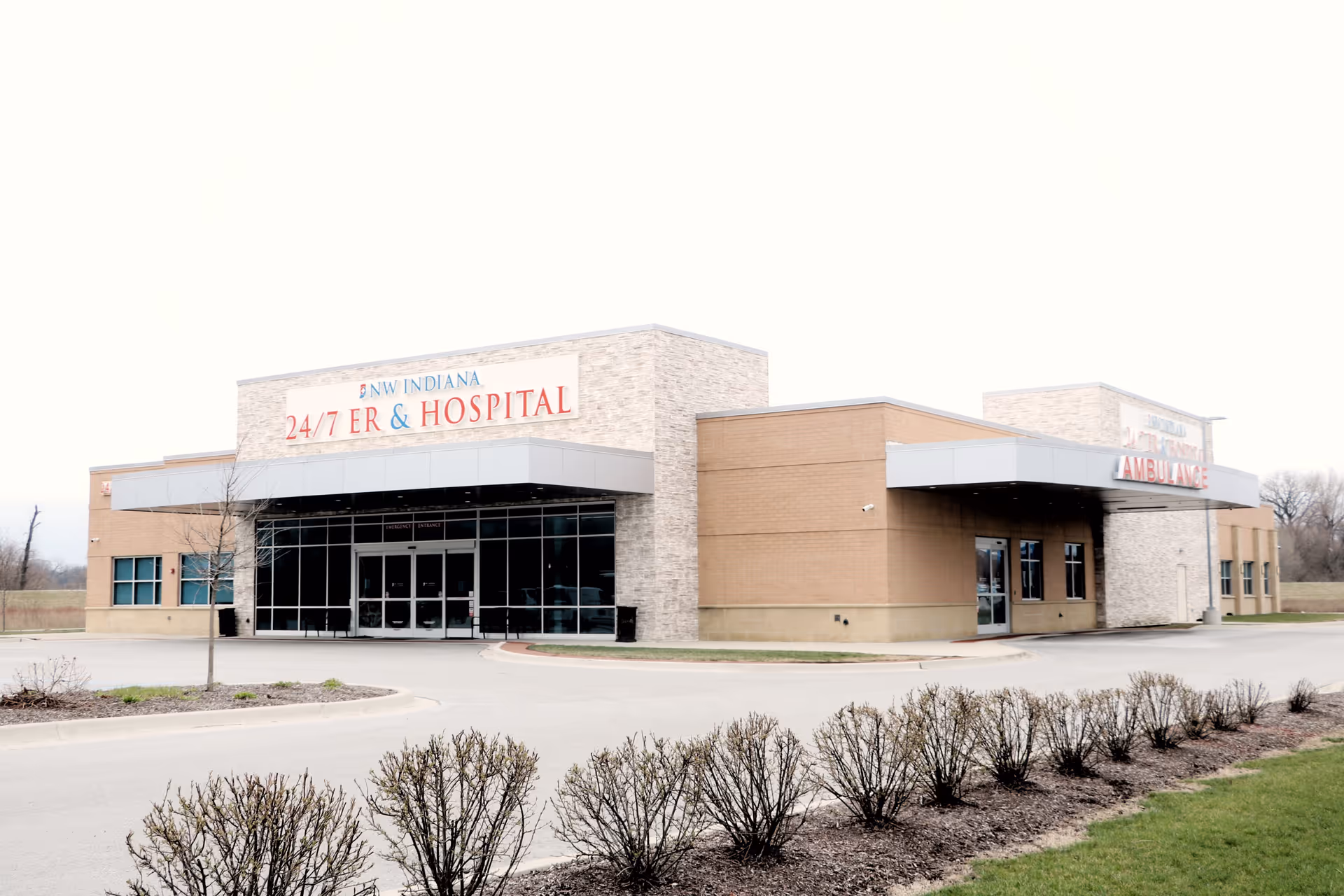 Exterior view of a modern medical facility marked 24/7 ER and Hospital with glass entry
