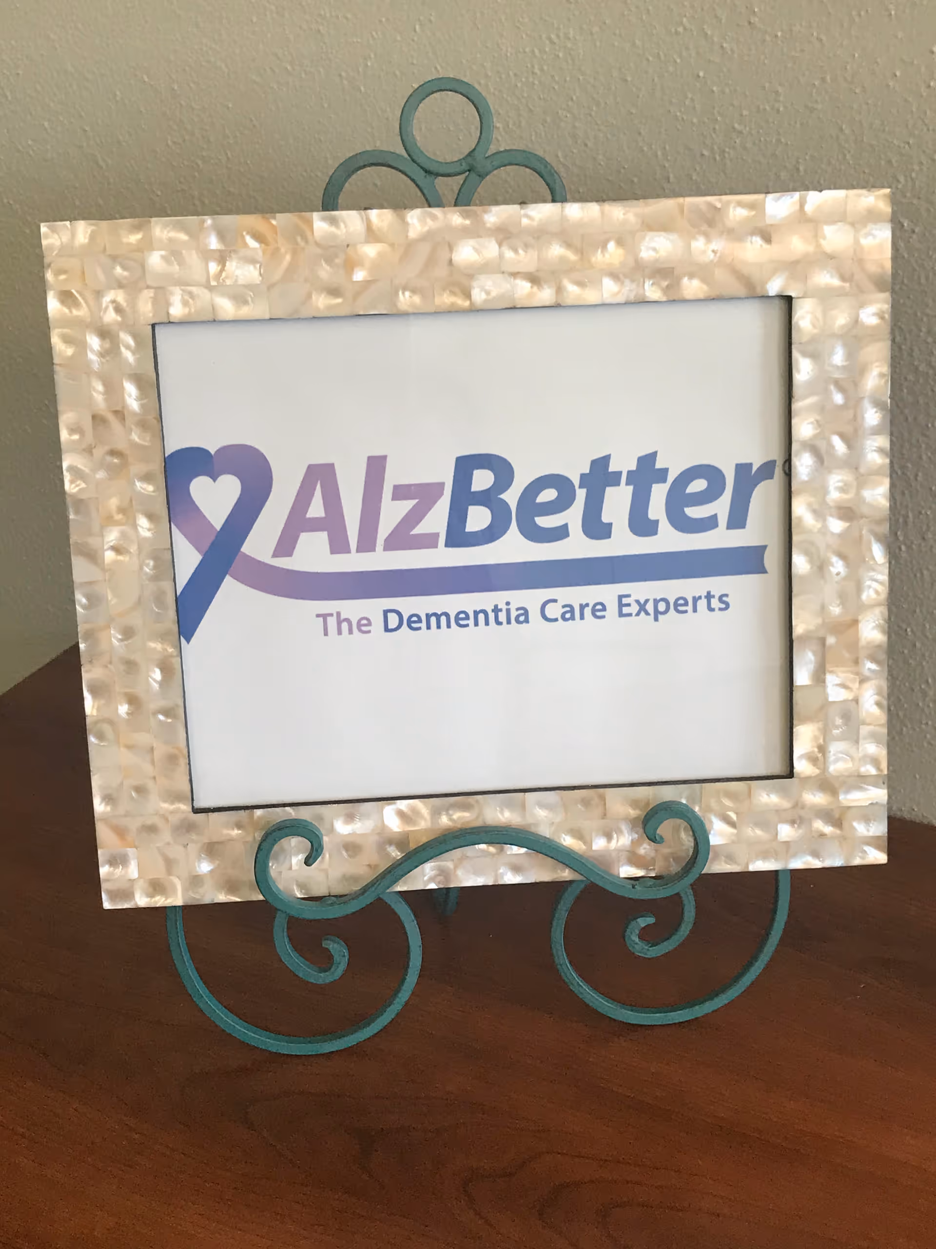 Decorative metal-framed sign on a wooden table reading AlzBetter The Dementia Care Experts
