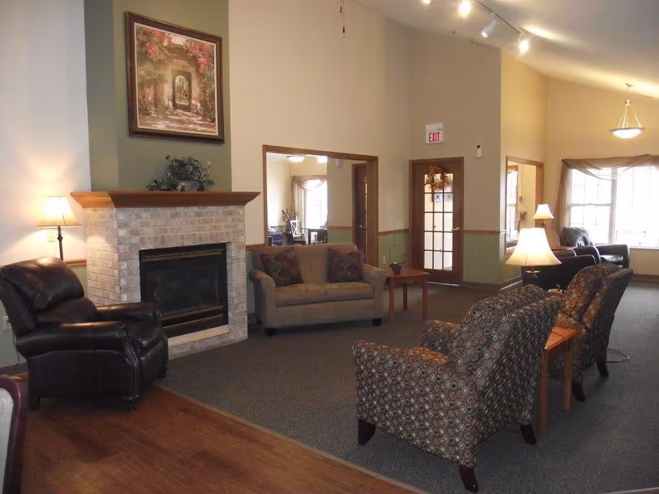 Communal living room with a brick fireplace, sofas and armchairs arranged around lamps and large windows.