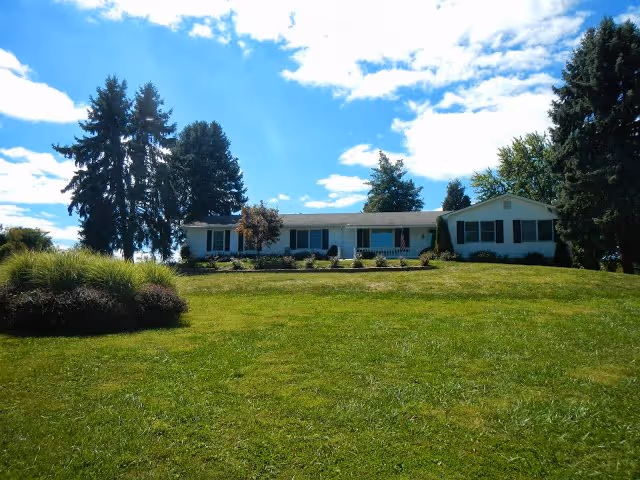 Front view of a single-story assisted living home on a grassy hill.