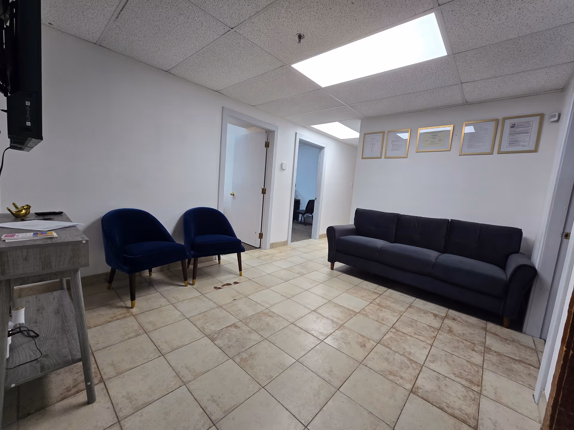 A facility waiting area with blue chairs, a dark sofa, and framed certificates on wall.