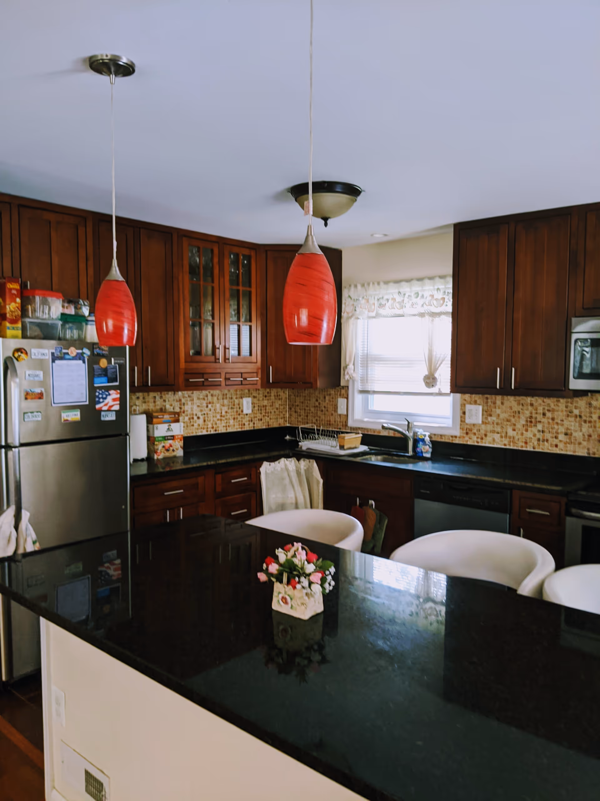 Modern kitchen with dark countertop island, wooden cabinets, and red pendant lights.