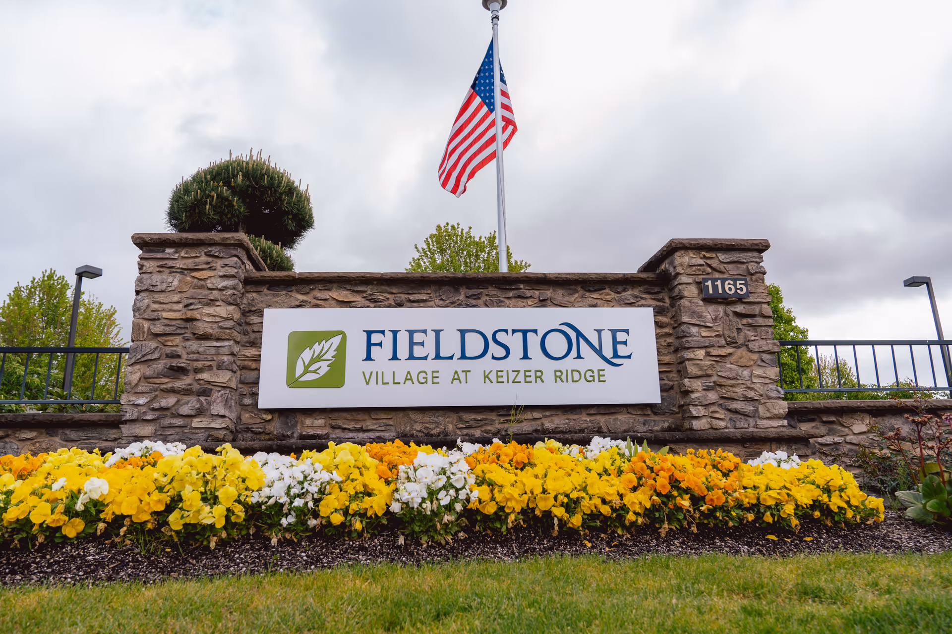 Stone entrance sign reads Fieldstone Village at Keizer Ridge, with flag and flowers.