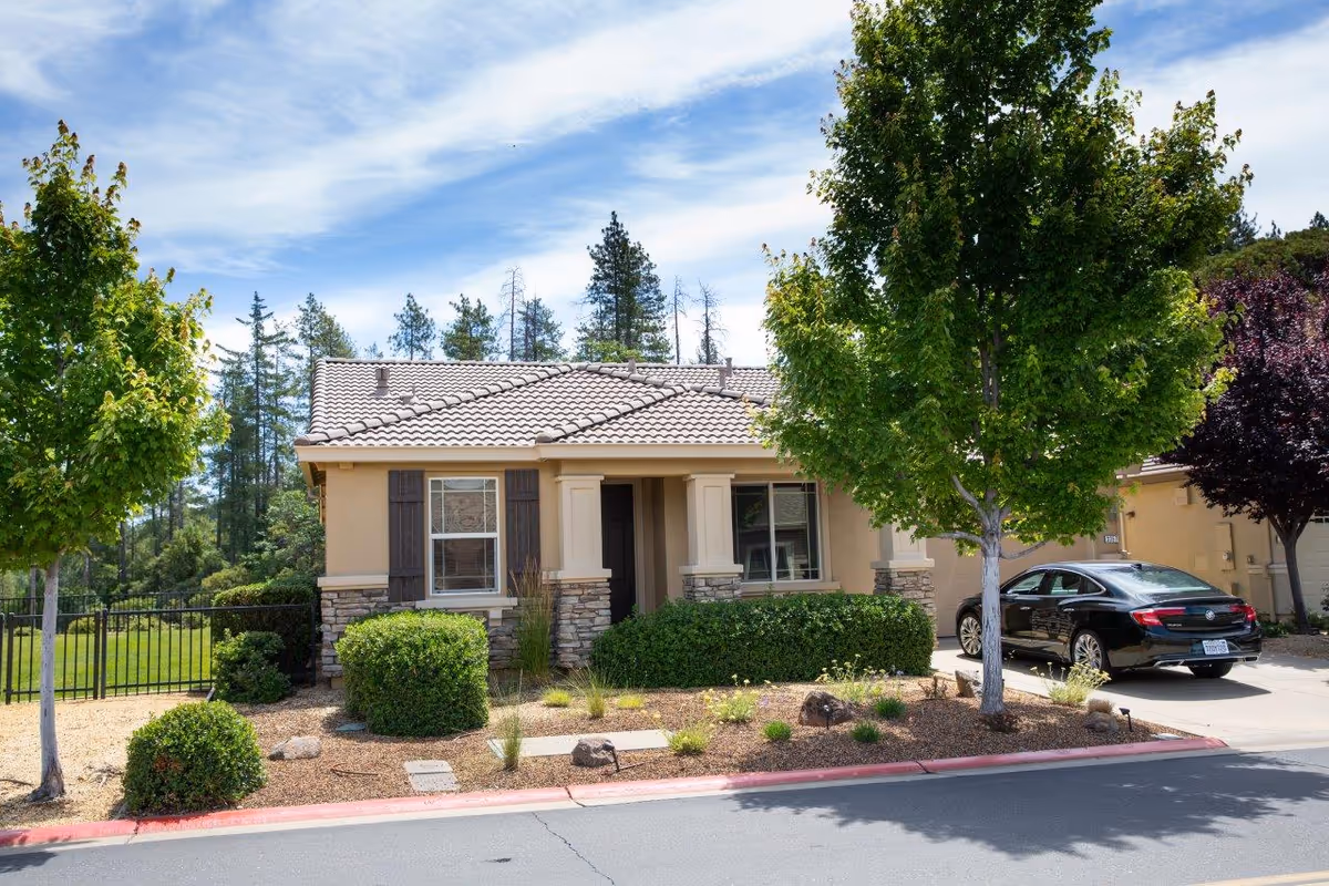Single-story beige senior facility exterior with tiled roof, landscaping, and a parked car.