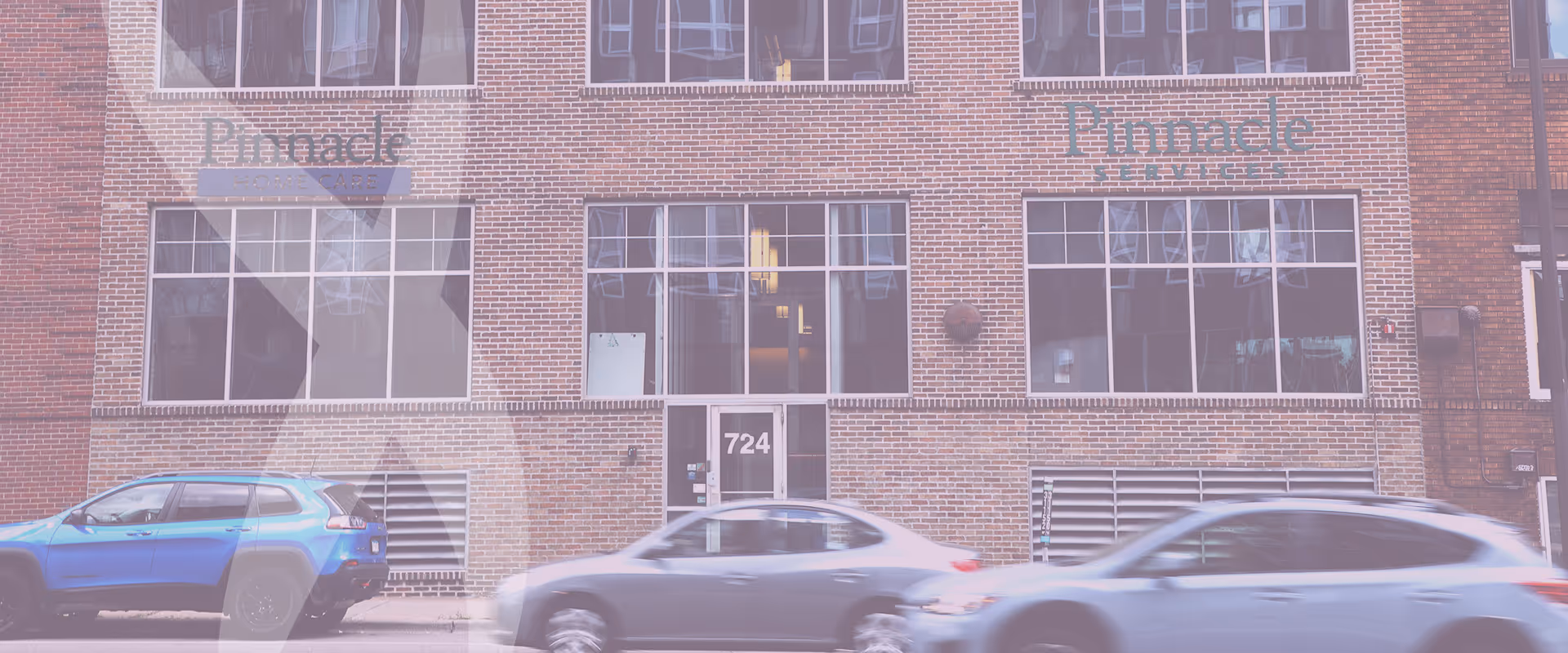 Brick building front with large windows, Pinnacle signs, and cars passing along the street.