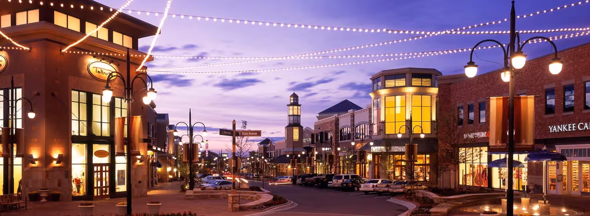 Twilight outdoor shopping street with string lights and illuminated storefronts.