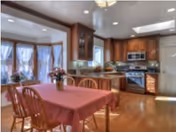 Cozy dining area with pink tablecloth, wooden chairs, and adjacent kitchen in warm wood tones.