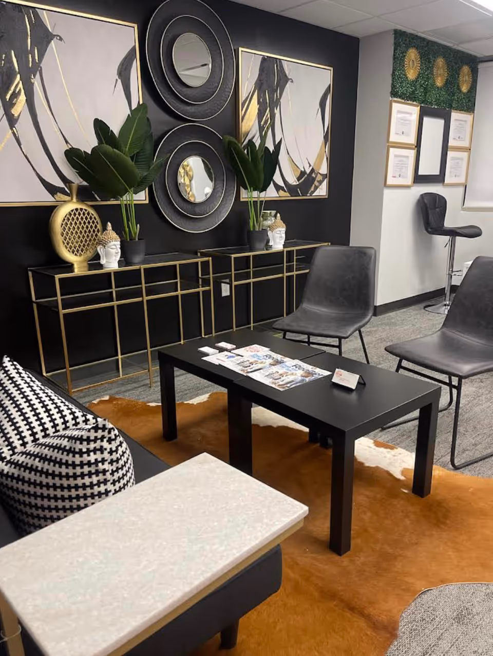 Modern facility lounge with black and gold decor, plants, and magazines on a coffee table.