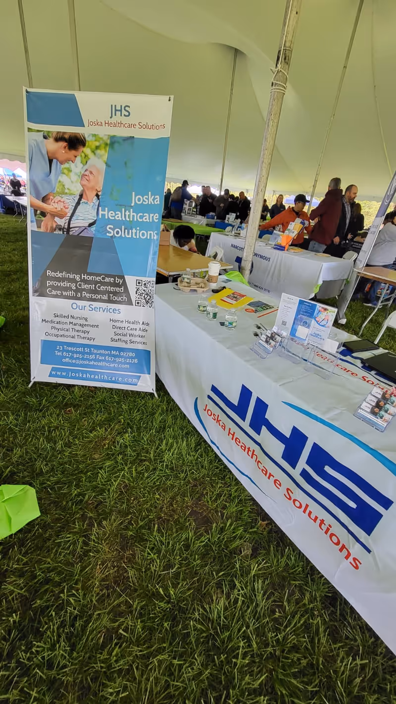 Exhibition booth inside a large tent with Joska Healthcare Solutions banners and attendees.