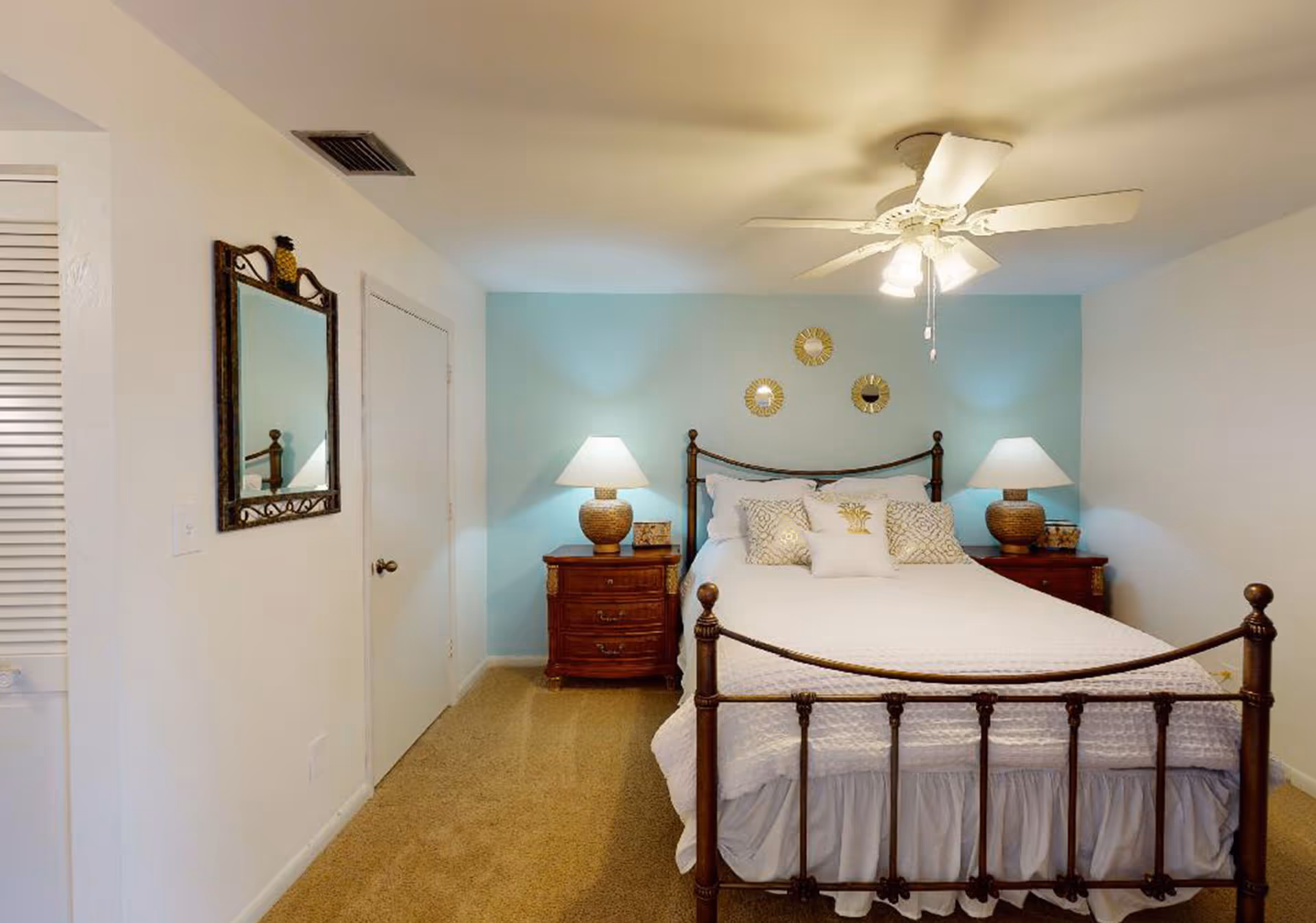 A neatly made bedroom with a metal bed, nightstands, lamps, and a blue accent wall.