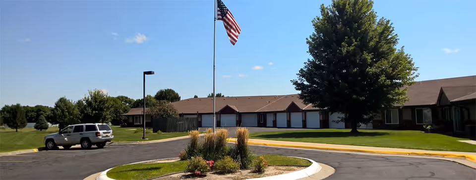 Exterior view of Regency Retirement Residence with flagpole, trees, and well-kept lawn.