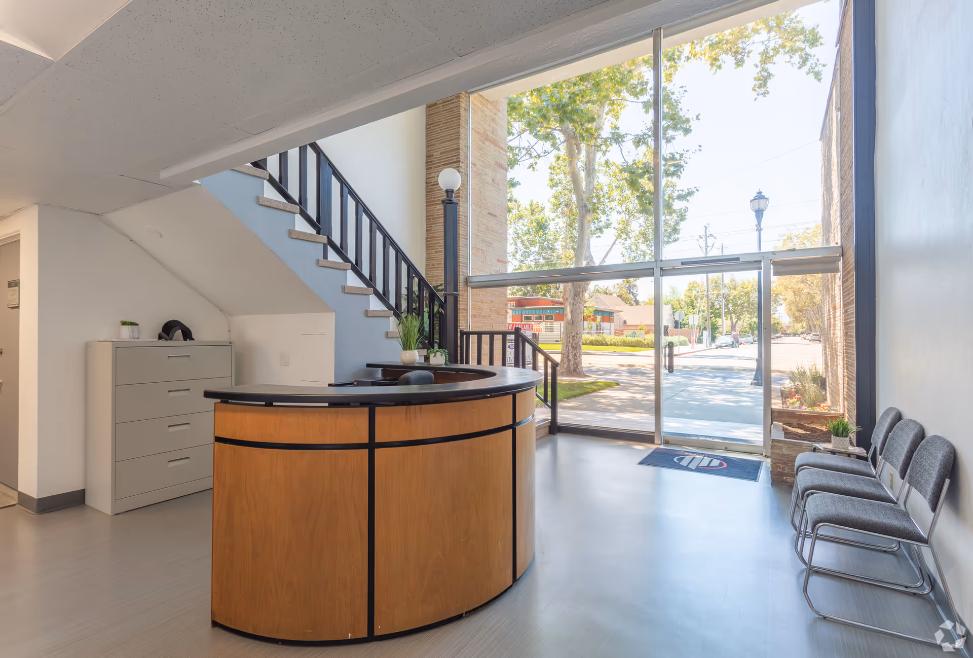 Interior reception area with curved wooden desk, stairs, glass doors, and waiting chairs