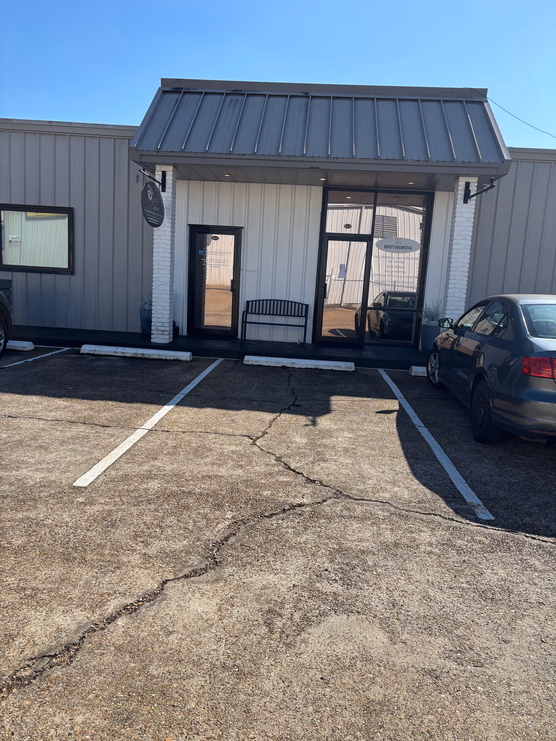 Front view of a gray facility with metal awning, glass doors, and parked cars.