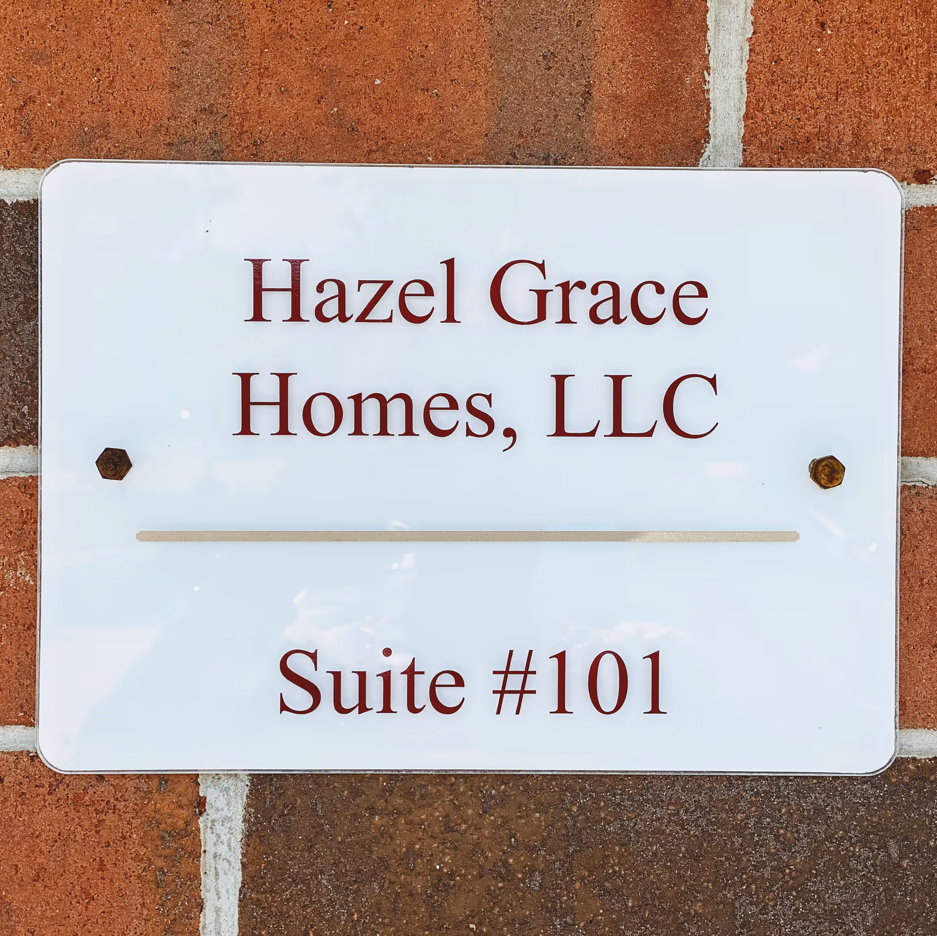 White sign on brick wall displaying Hazel Grace Homes, LLC, Suite #101.