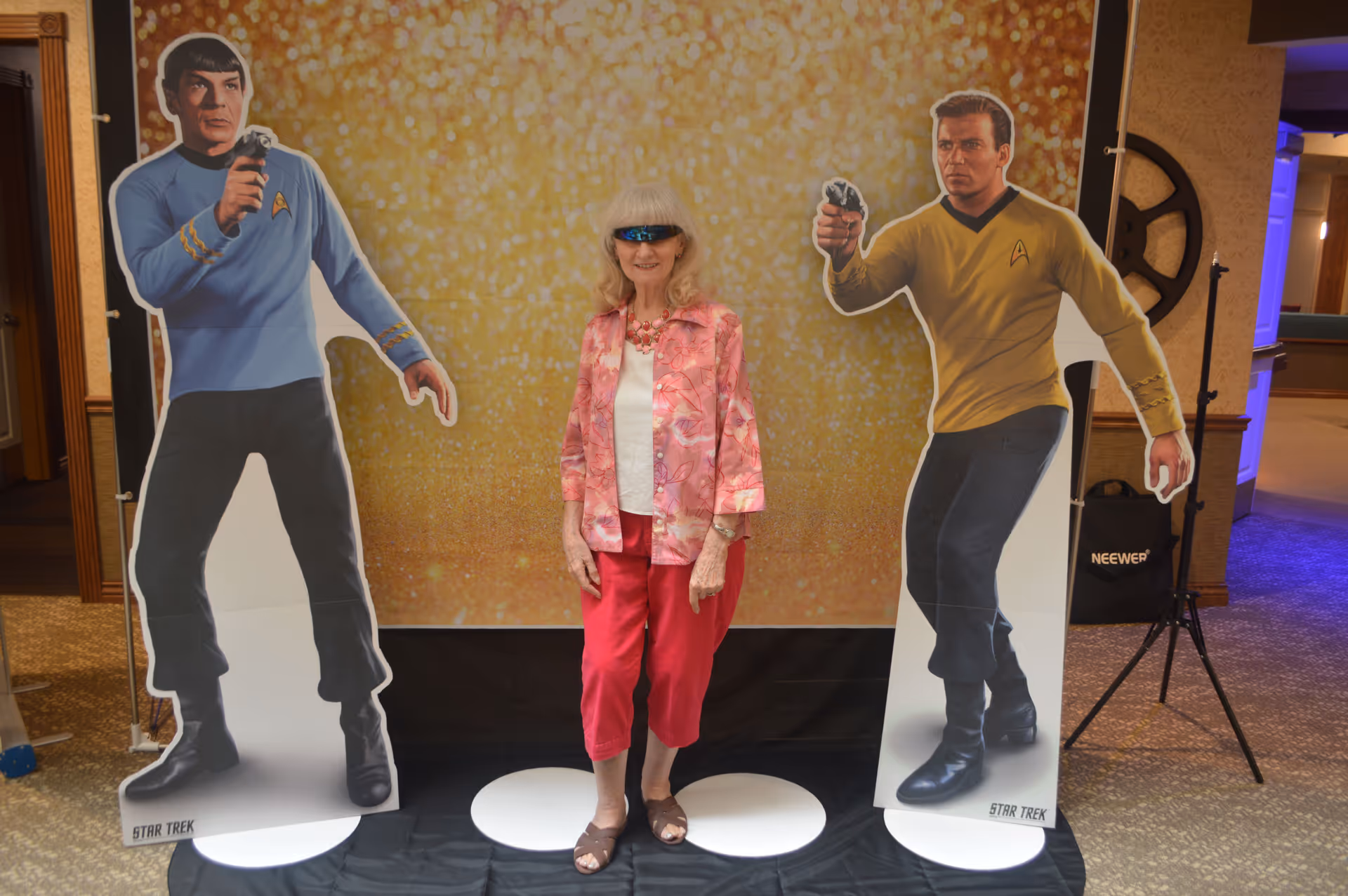 Senior woman posing between life-size Star Trek cutouts in a decorated indoor lobby.