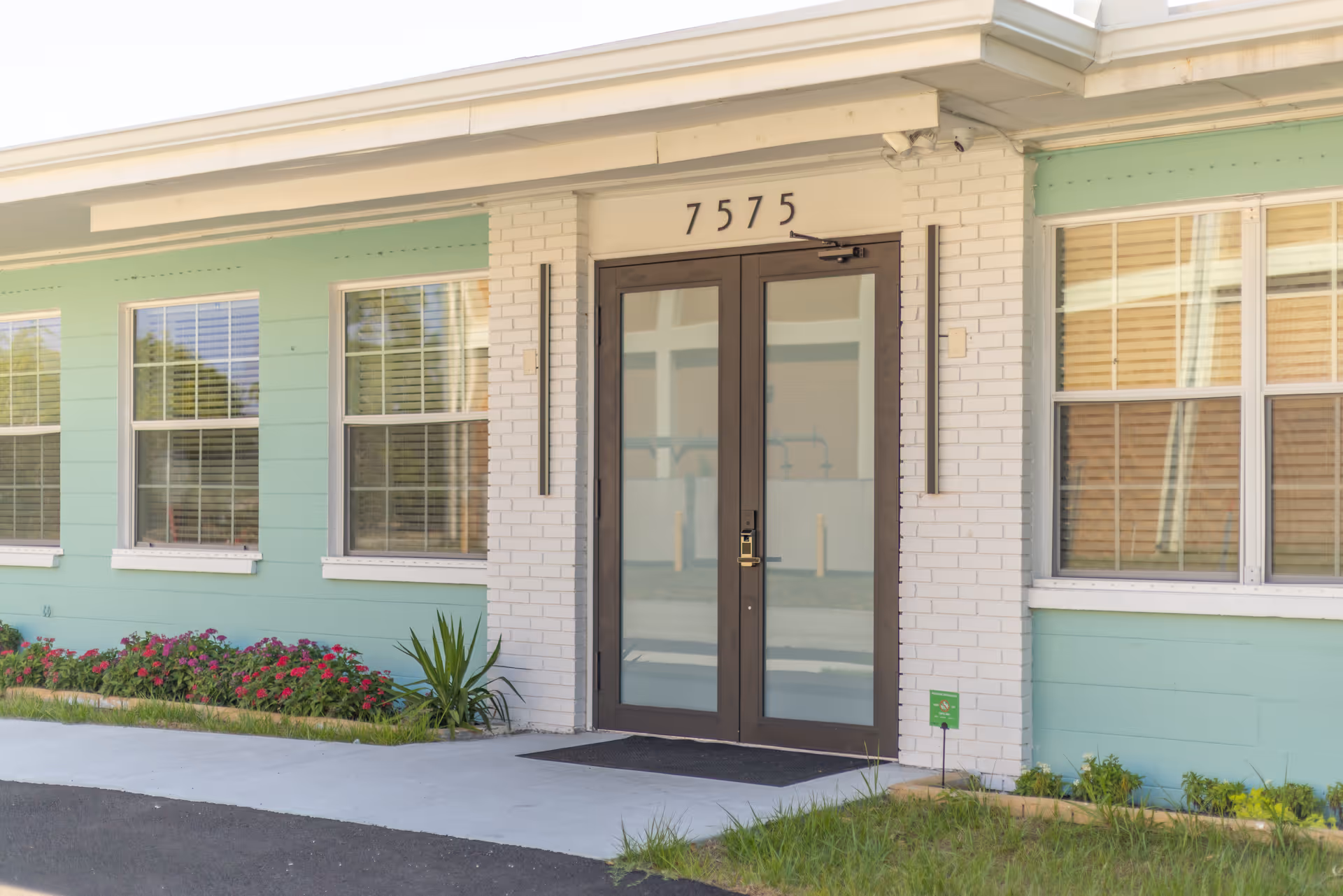 Front entrance of a pastel-green senior living facility with glass doors and landscaping.