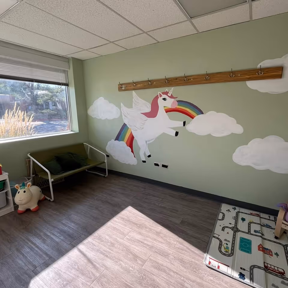 Colorful unicorn mural on the wall with a rainbow, small bench, and toys in a playroom.