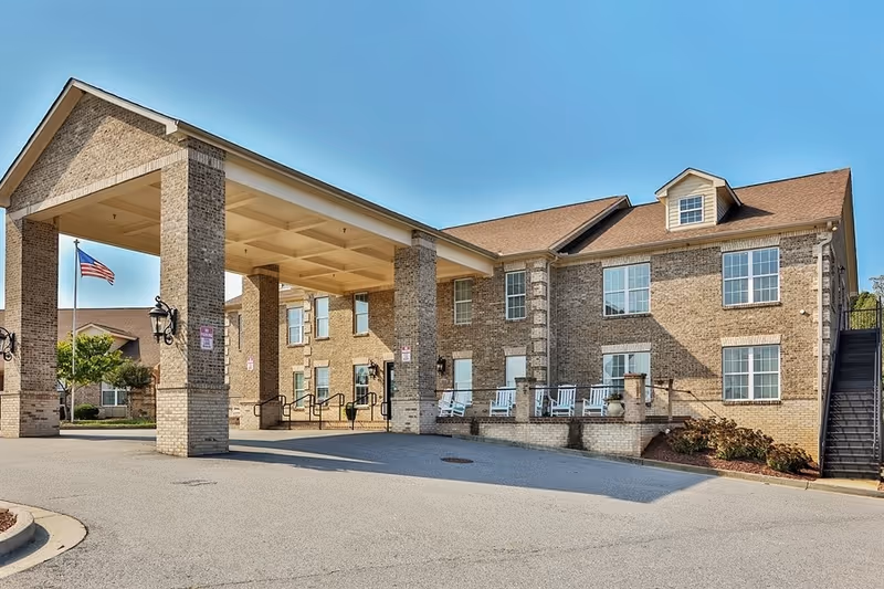 Brick senior-living facility with porte-cochère entrance and rocking chairs on the front porch.