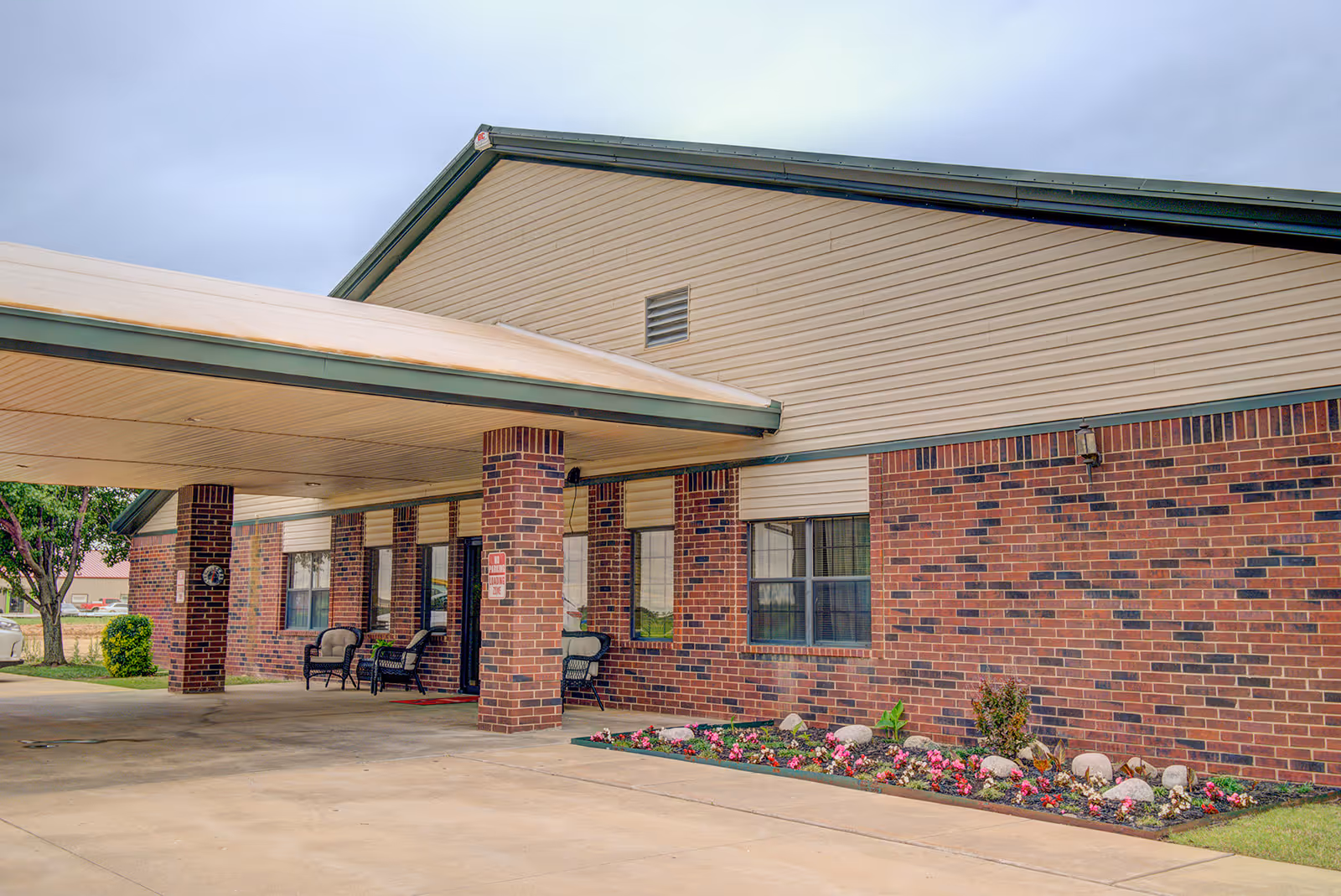 Brick exterior of a senior living facility with a covered entrance and seating.