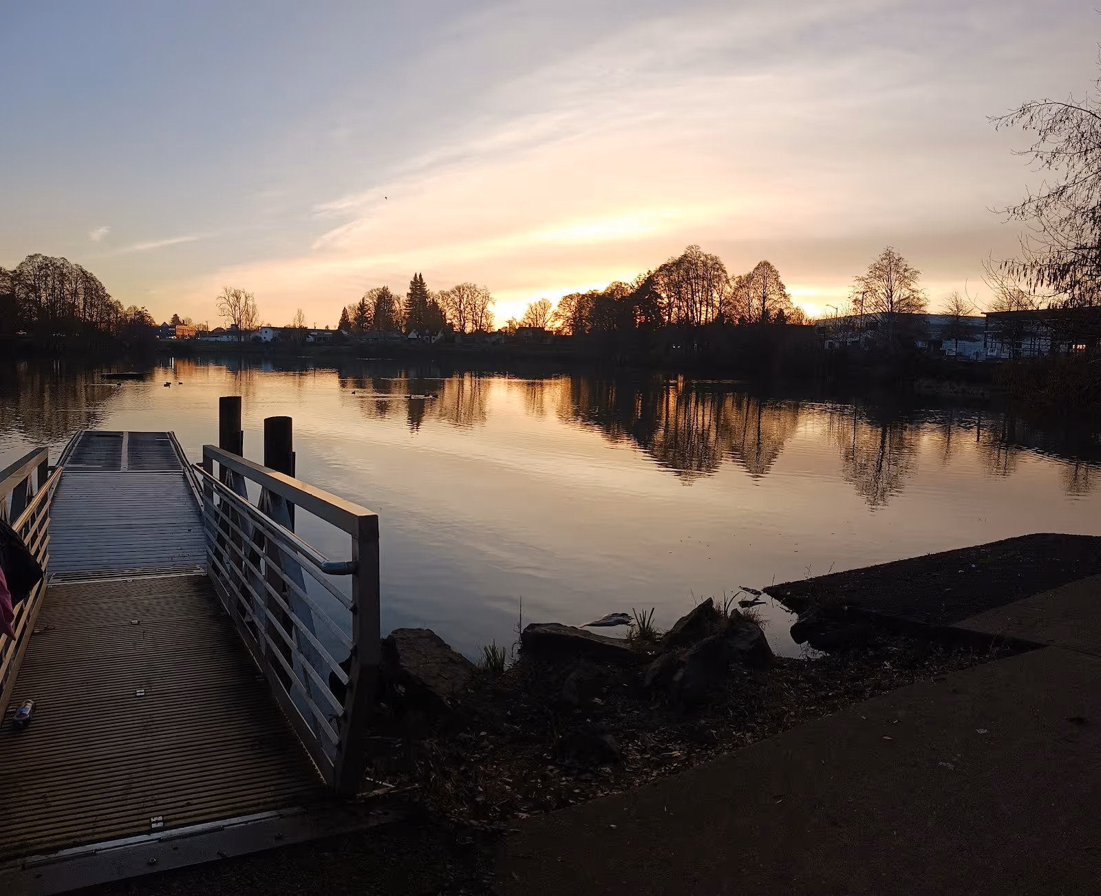 Sunset over a calm lake with a wooden dock and trees along the shore