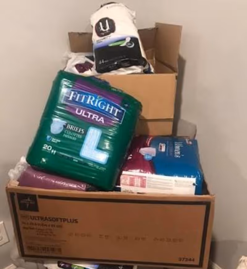 Box filled with diaper packs and supplies in a small storage corner.