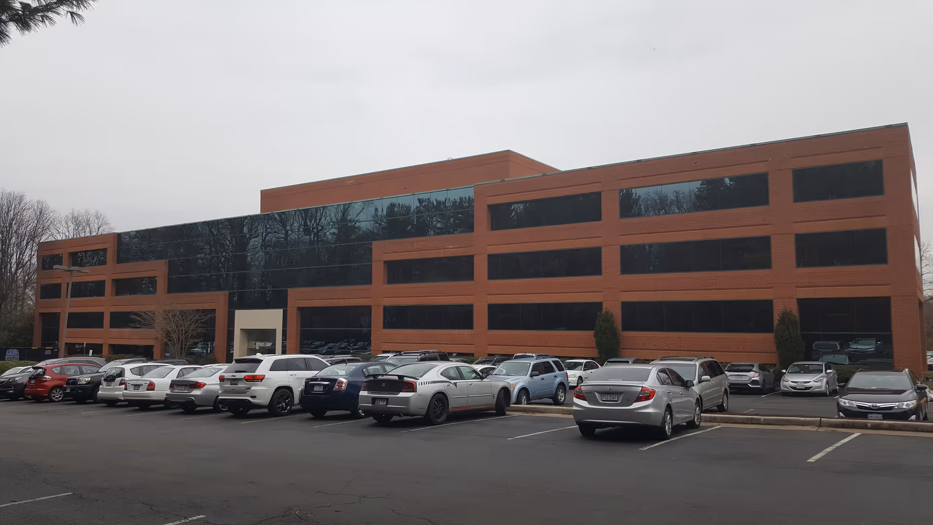 Brick office building with large dark windows and a front parking lot.