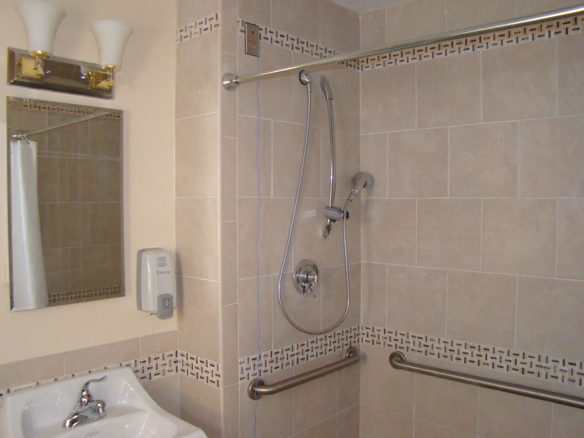 Accessible bathroom with tiled walls, handheld shower, grab bars, mirror, and sink.