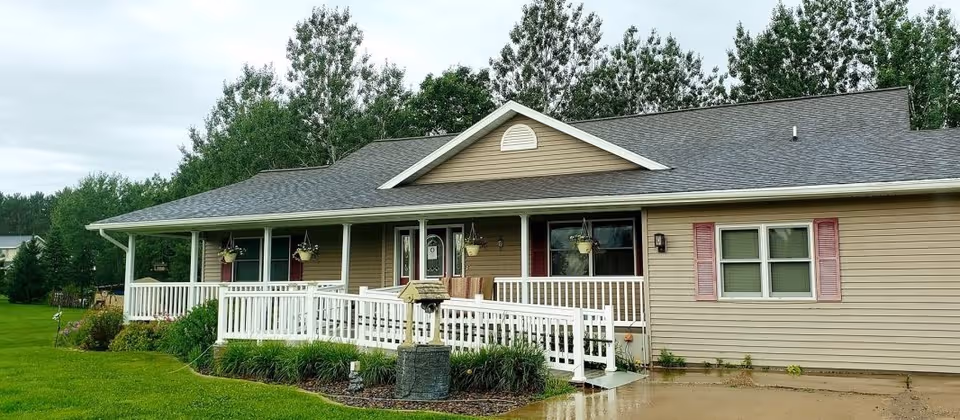 Single-story beige senior living facility with a wide covered porch and white railing.