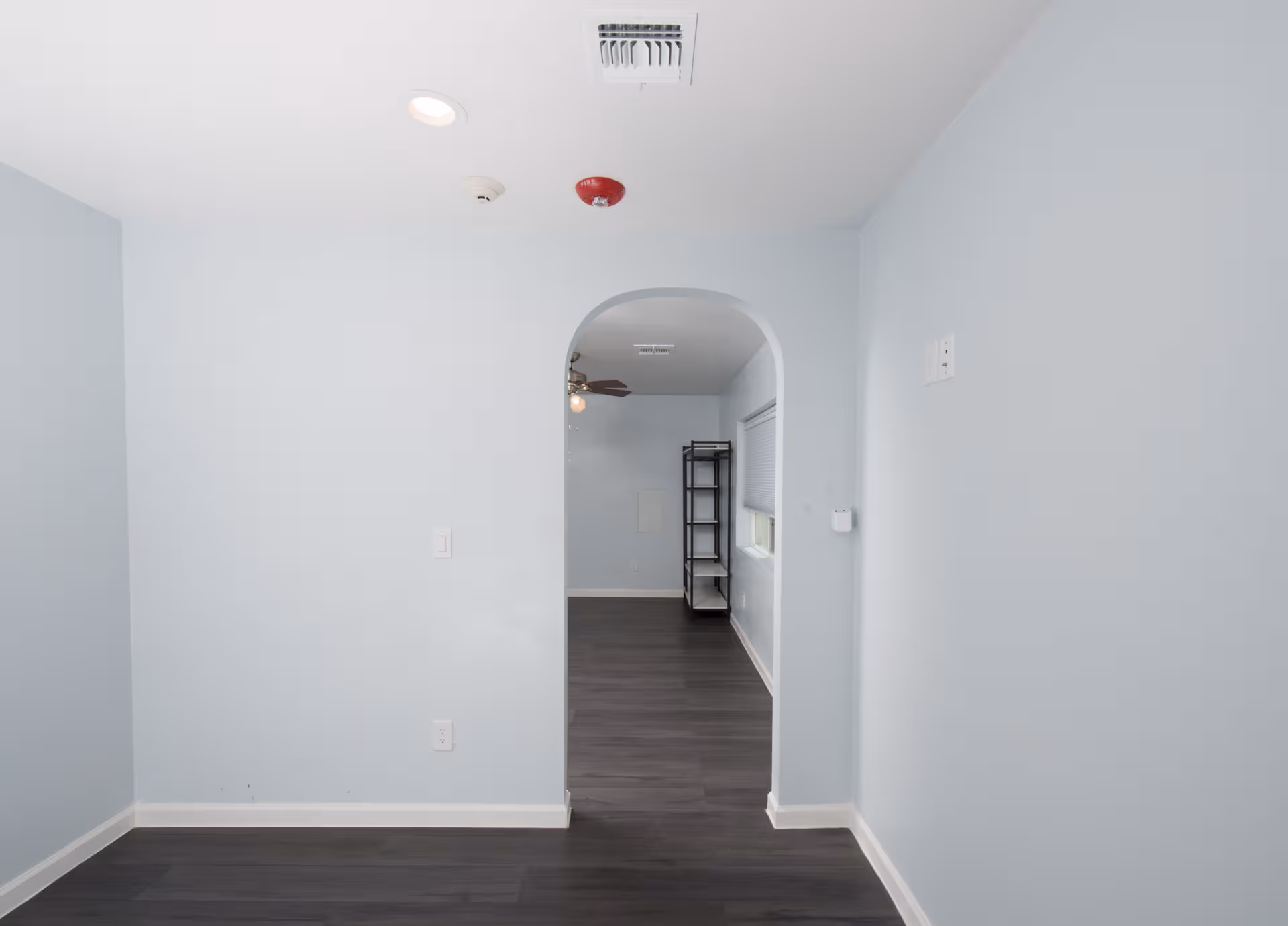 Light blue interior hallway with an arched doorway and metal shelving.