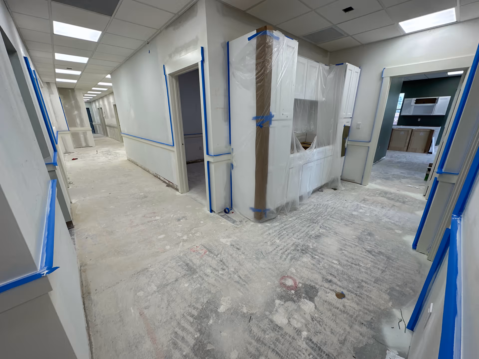 Interior hallway under renovation with plastic-wrapped doorways and blue tape.