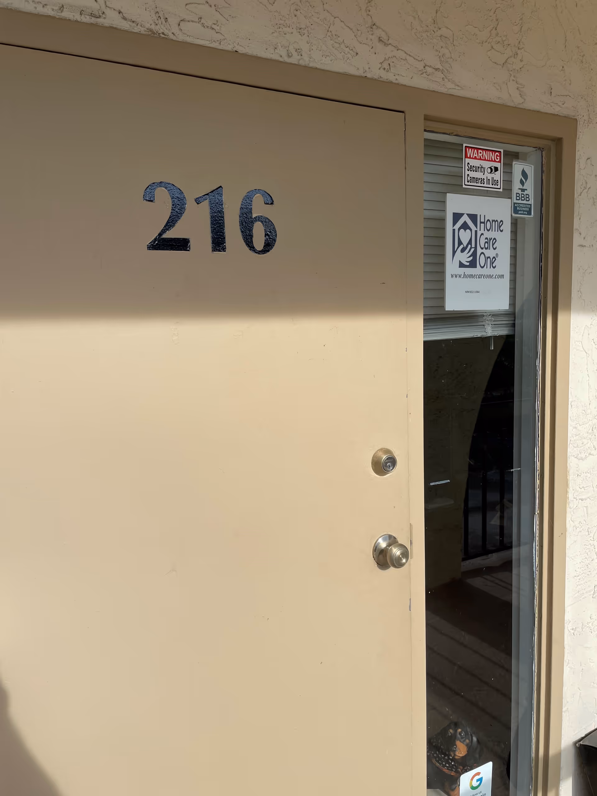 Beige exterior entry door marked 216 beside glass panel with Home Care One sign.
