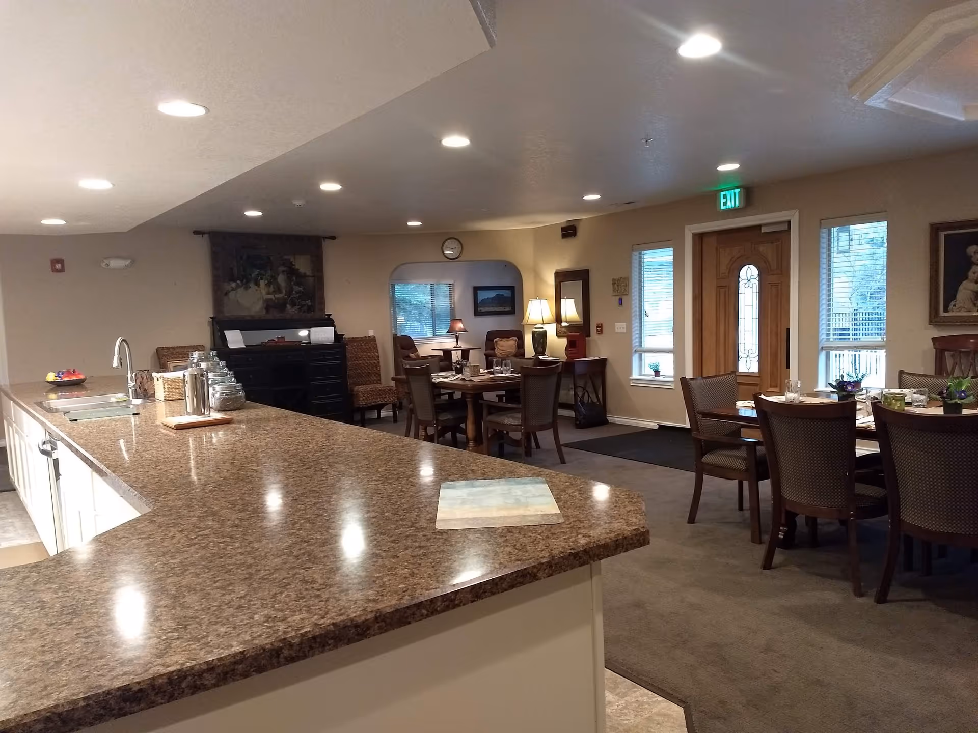 Interior common area with granite counter, dining tables, chairs, and an exit door.