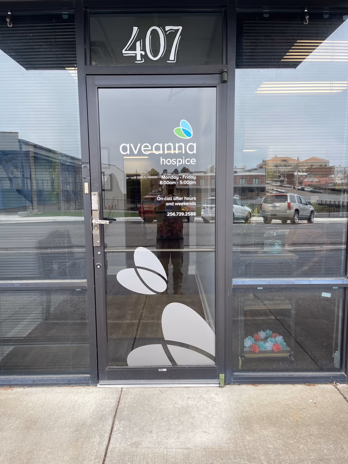 Glass entrance door displays Aveanna Hospice logo, building number 407, with reflections of the parking lot.