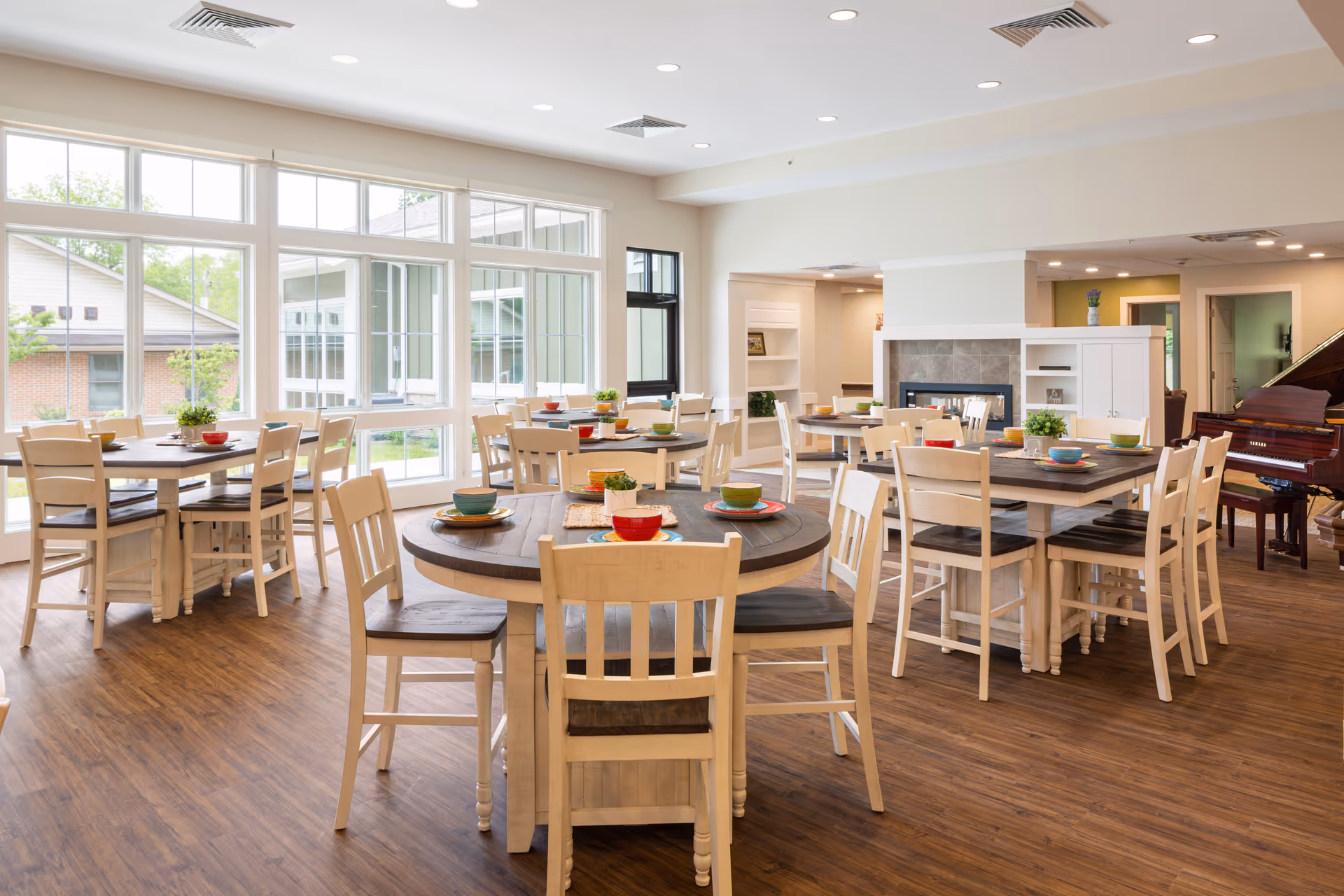 Bright senior living dining room with round and rectangular tables, chairs, and colorful place settings.