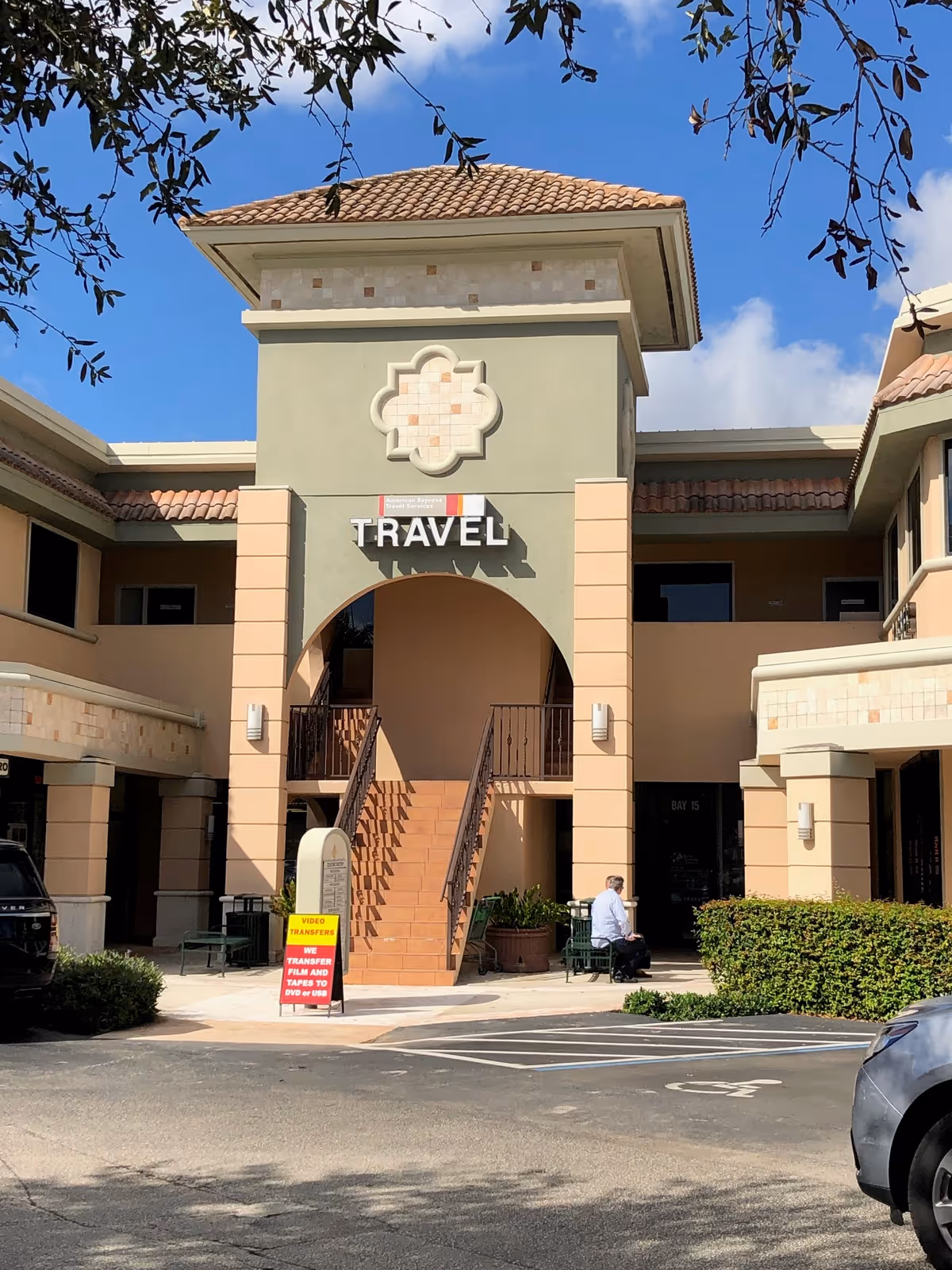 Front facade of a beige travel agency building with arches, stairs, and decorative tile.