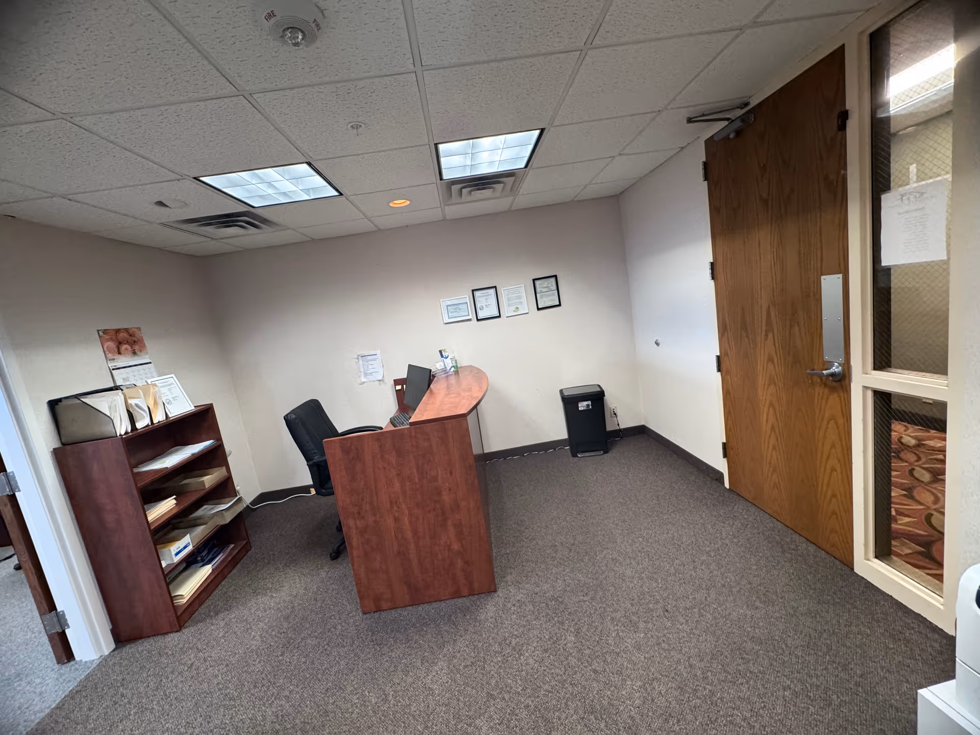 Reception desk with chair, bookshelf, certificates on wall in a small office.