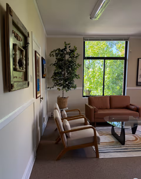 Cozy lounge area with a sofa, two armchairs, glass coffee table, and a plant.