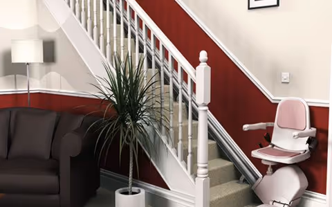 Interior hallway with staircase, red wall, sofa, plant, lamp, and stairlift chair